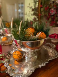 a silver bowl filled with oranges sitting on top of a metal tray next to christmas decorations