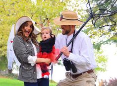 a man and woman holding a baby while standing next to each other in the grass