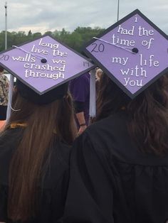 two graduates wearing purple caps and gowns with writing on them at the graduation ceremony