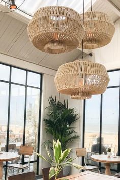 a dining room with large windows and wicker chandeliers hanging from the ceiling