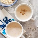 two cups of coffee sitting on top of a blue and white napkin next to a bowl of oatmeal