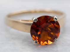 a ring with a large orange stone on it's shants, sitting on a white surface