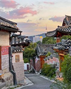 an alley way with buildings and trees on both sides at sunset in the background, there is a pink sky