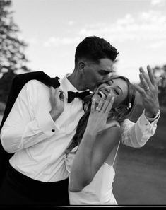 a man and woman kissing each other while standing next to each other in front of trees