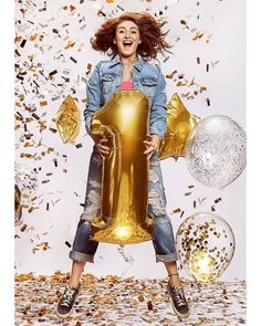 a woman holding a giant golden balloon in front of confetti