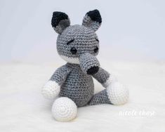 a crocheted gray and white stuffed animal sitting on top of a fluffy blanket