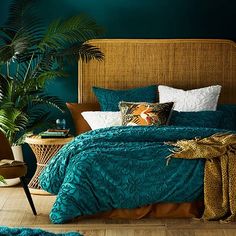 a bed with blue comforter and pillows next to a potted plant in the corner