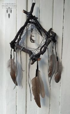 a dream catcher with feathers hanging from it's side on a white wooden wall