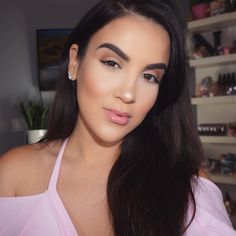 a woman with long dark hair wearing a pink top and diamond earrings is looking at the camera