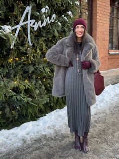 a woman standing in front of a christmas tree wearing a gray dress and fur coat