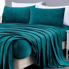 a bed covered in a teal blanket and pillows with two white nightstands next to it