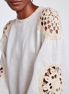 a woman wearing a white shirt with crochet on the sleeves