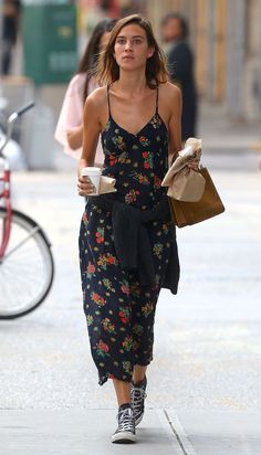 a woman walking down the street holding a coffee cup and paper bag in her hand