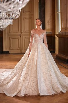 a woman in a white wedding dress standing on a wooden floor with chandelier