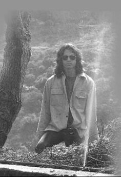 black and white photograph of a man standing in front of a tree with his hands on his hips