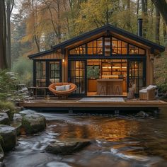 a small cabin in the middle of a forest with a river running through it and lots of trees around