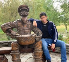 a man sitting on top of a wooden bench next to a statue of an old man