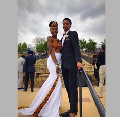 a man and woman standing next to each other in front of some stairs with people looking on