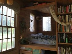 there is a bed in the room with many books on it and two windows that are open