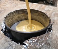 a bowl filled with yellow liquid being poured into the bowl on top of a wooden table