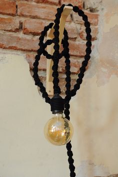 a light bulb hanging from the side of a brick wall next to a roped cord