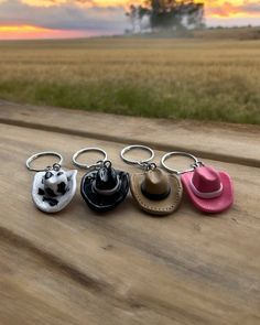 four keychains with hats on them sitting on a wooden table in front of an open field