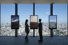 two people standing in front of large windows looking at cityscape and skyscrapers