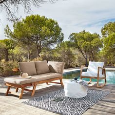 two chairs and a couch on a deck next to a pool with trees in the background