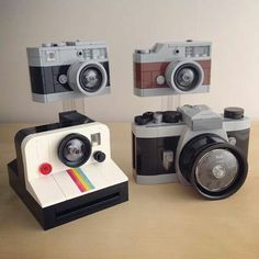 three lego cameras sitting next to each other on top of a wooden table and one has a polaroid camera in front of it