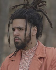 a man with dreadlocks in an orange jacket looking at the camera while standing outside