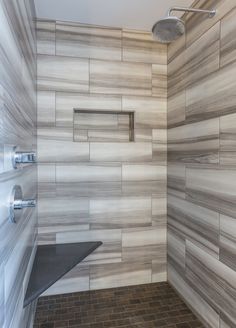 a walk in shower sitting next to a tiled wall and floor with gray tile on the walls