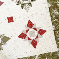 a quilted table topper with red and green stars on the center, surrounded by white flowers