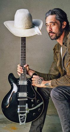 a man with a hat on his head is holding a guitar and posing for the camera