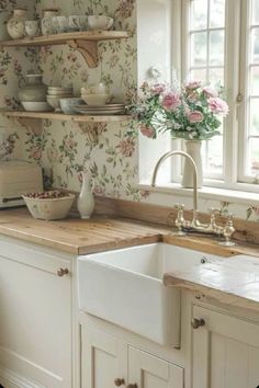 a white kitchen sink sitting under a window next to a wooden counter top with flowers on it