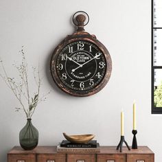 a clock on the wall above a dresser with candles and vases in front of it