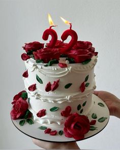 a white cake with red roses on it and two candles in the shape of numbers