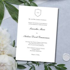 a wedding card with white flowers and greenery on the side, next to it