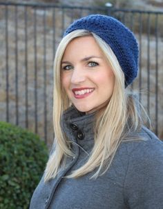 a woman with blonde hair wearing a blue hat and gray coat smiling at the camera