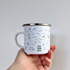 a hand holding a white and green enamel coffee cup with illustrated designs on the inside