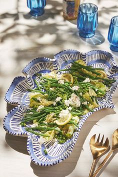 a plate with asparagus and cheese on it next to blue glassware, silverware and utensils