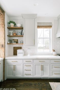 a kitchen with white cabinets and open shelves on the wall, along with wooden flooring