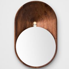 a round mirror mounted to the side of a wooden wall hanging on a white wall