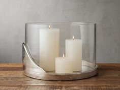 three white candles in a glass container on a wooden table