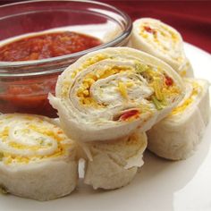 there are several rolls on the plate with salsa in the bowl behind it and sauce