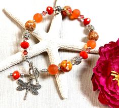 a white starfish with orange beads and charms on it next to a pink flower