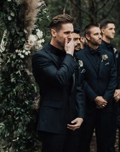 a group of men standing next to each other in front of a lush green forest