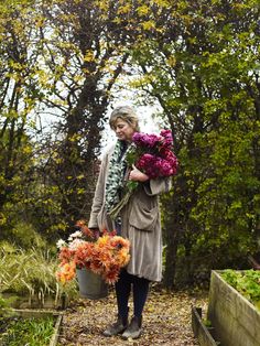 a woman holding flowers in her hands while walking down a path through the woods on a fall day