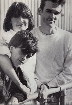 three people standing next to each other in front of a fence with their arms around one another