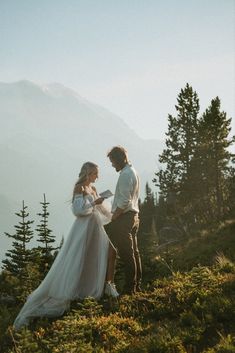 a man and woman standing on top of a mountain next to each other holding hands