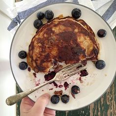 a pancake on a plate with blueberries and syrup is being held by a hand